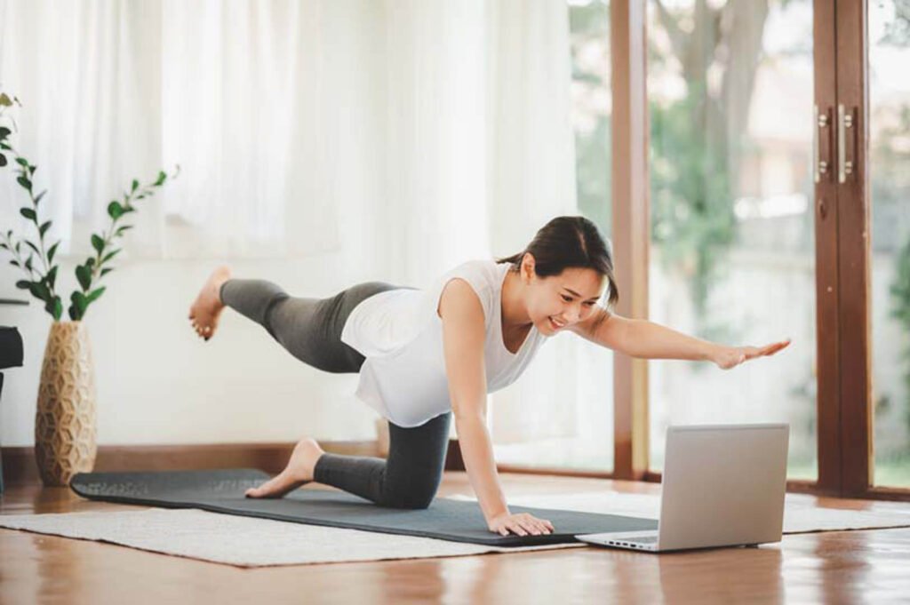 Woman exercising at home using her laptop