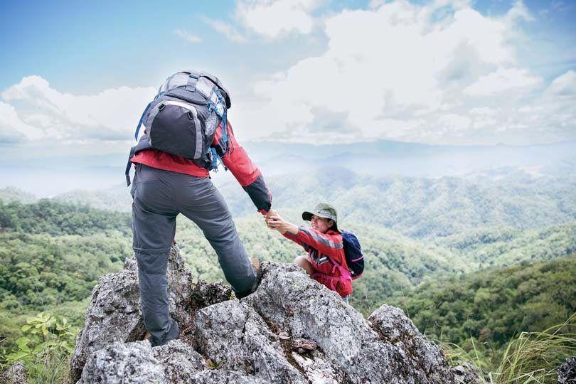 Man and woman giving a helping hand while hiking up a mountain